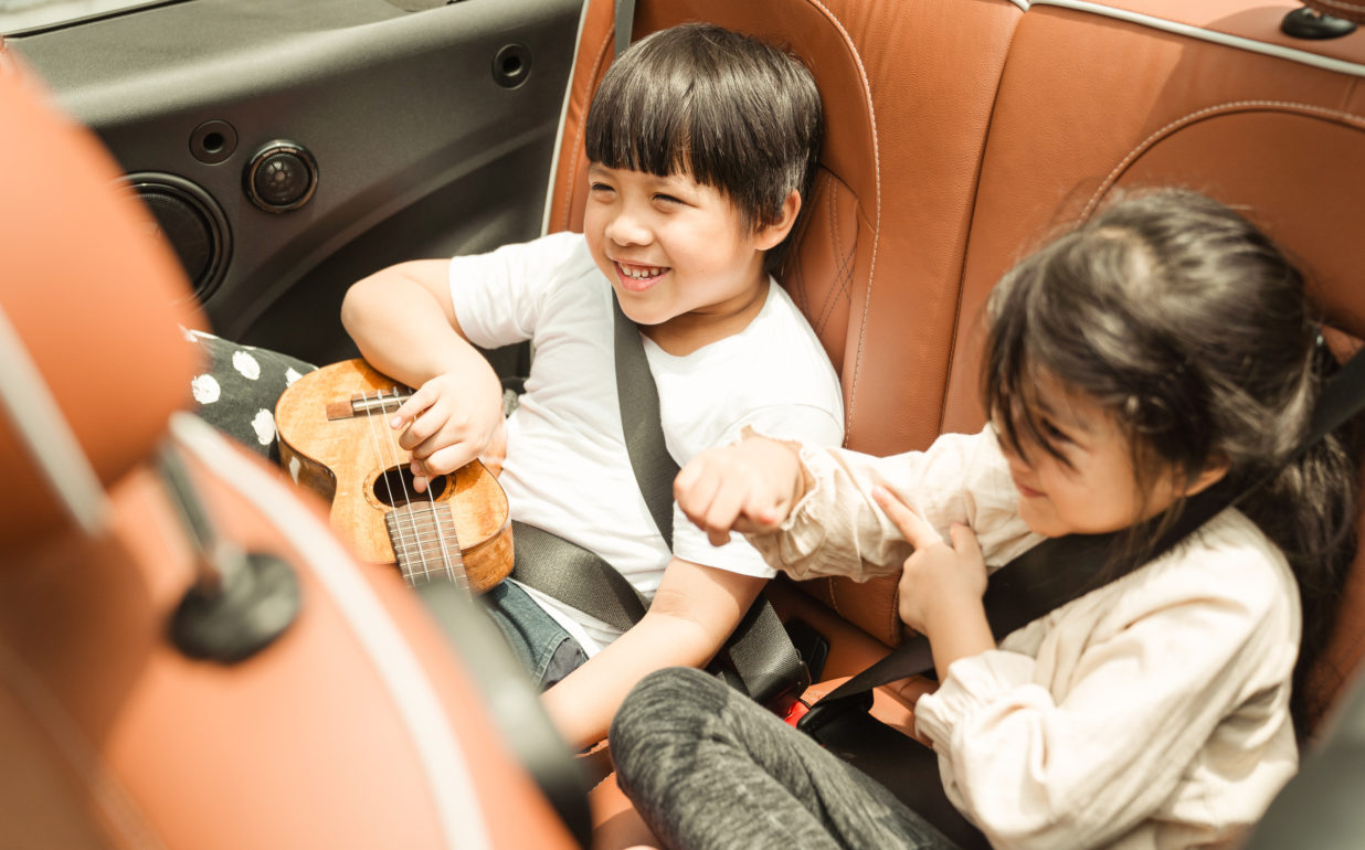 Two Young Kids Enjoying Road Trip in Back Seat of Car Children smiling in backseat of car, safe with Onust vehicle protection plan