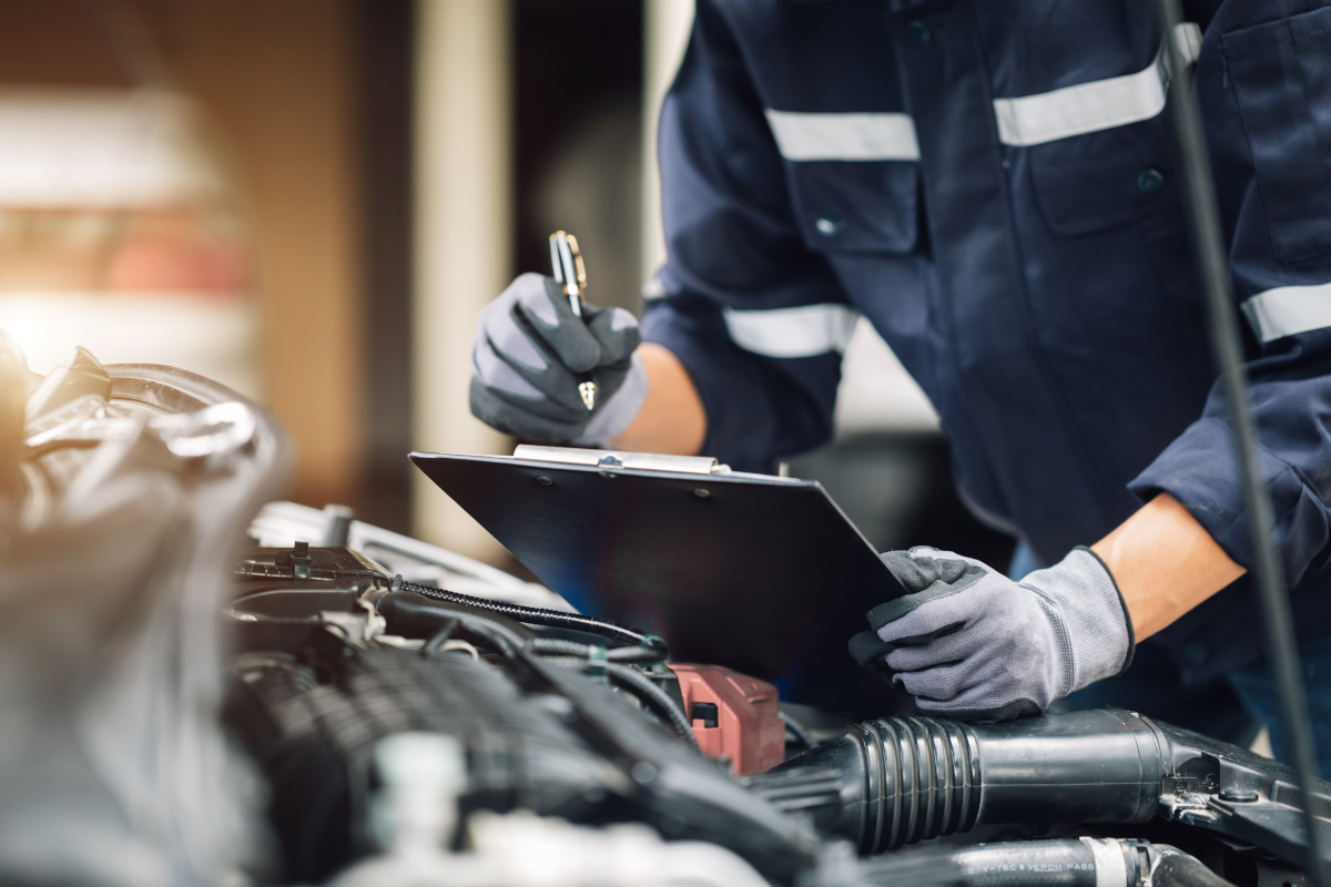 Mechanic Holding Clipboard Inspecting Car Mechanic checking engine and writing on clipboard, covered by Onust extended warranty